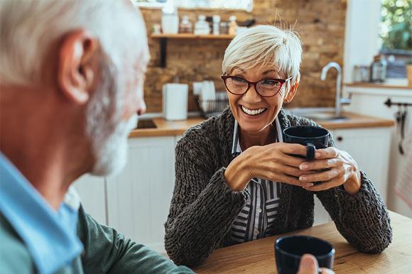 Older couple chatting and drinking tea at home in Radcliffe